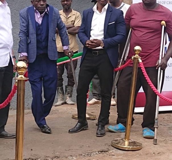 KPDDI members at a dedication moment outside a building in Kireka, two using crutches