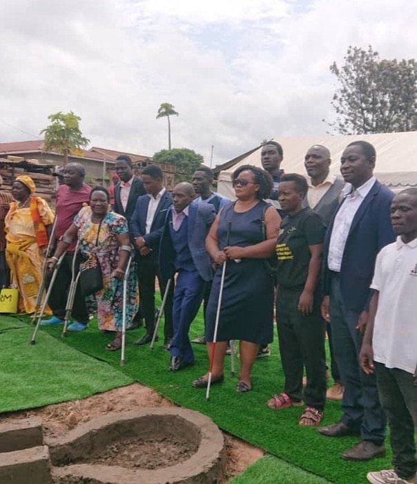 KPDDI members and visiting partners standing together at the new borehole in Kireka; several use crutches and one a white cane