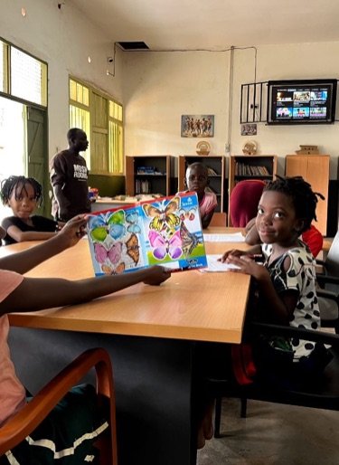 Children reading together at a table in KPDDI's community library in Kireka; a boy holds up a picture book of butterflies