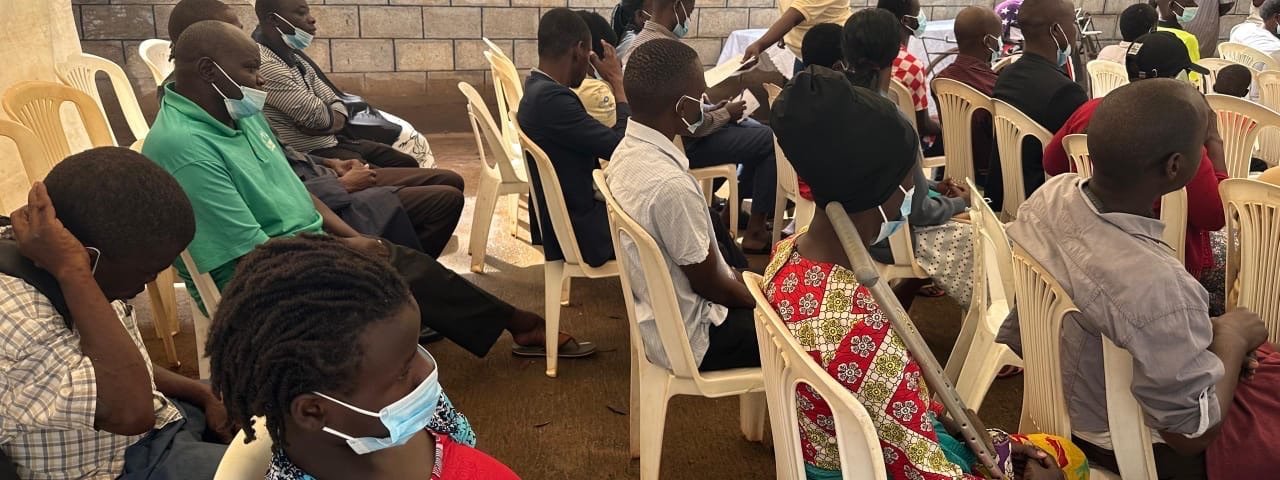 Community members seated under a tent at a KPDDI meeting in Kireka
