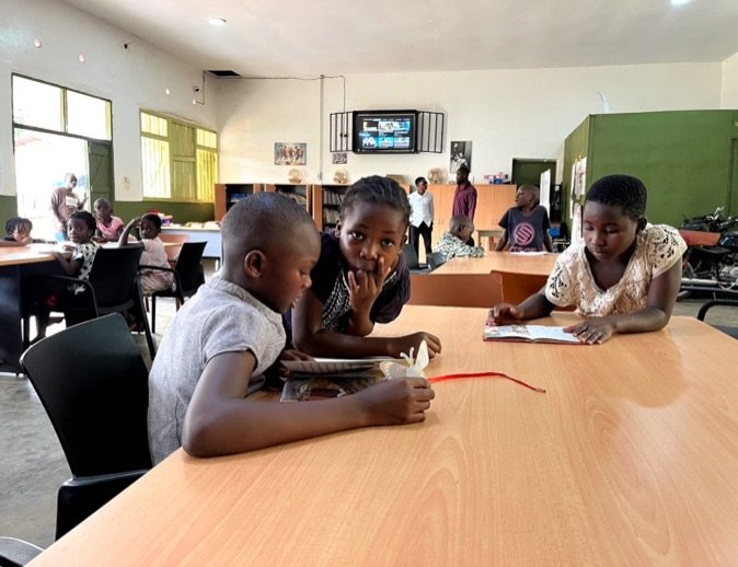 Three children reading books together at a table in KPDDI's community library