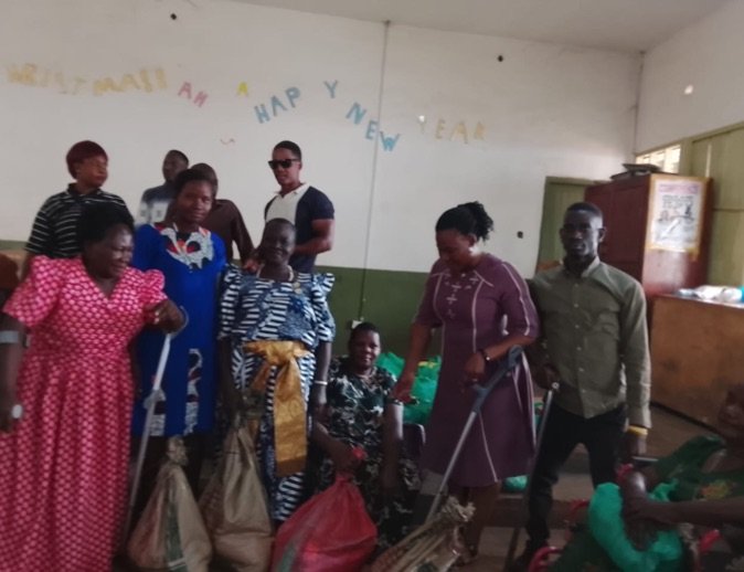 Women members of KPDDI, several using crutches, standing together at a support distribution in the community hall