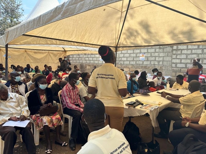 Community members seated under white tents at an awareness meeting at KPDDI in Kireka
